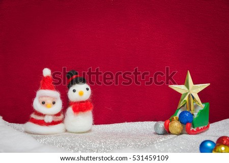 Santa claus, snowman wool doll, greed sled on snow set up with glittering christmas ball, shiny star decoration with red cloth backdrop, happy new year and christmas concept background