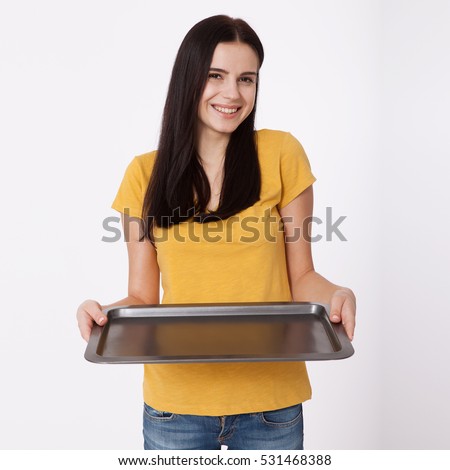 Young attractive woman holding an empty tray isolated on white background. Woman in yellow T-shirt friendly smiles. Blank template for design of the tray. Royalty-Free Stock Photo #531468388