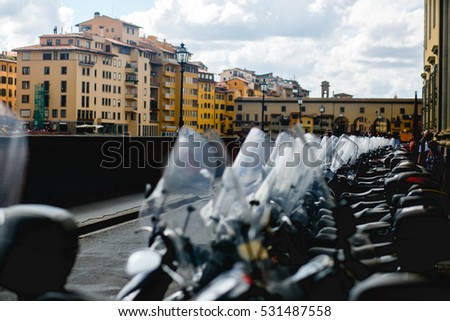 Scooters and motorcycles stand in the ray along the stone bridge