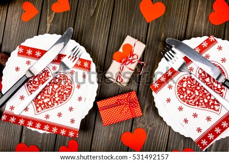 Little present boxes decorated with paper hearts lie among white plates on wooden dinner table