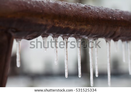 Icicles hanging from a brown pipe. Frozen water and metal surface, winter time concept. selective focus shallow depth of field