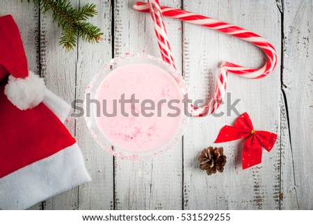 Traditional Christmas pink cocktail candy cane punch in glass, decorated with shards of candy. On a white wooden table, top view, surrounded by Christmas decorations and Santa hats, selective focus 