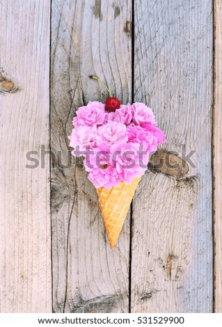 Flowers composition - pink roses flowers and cherry in ice cream cone on rustic wooden background. Stylish flat lay. Minimal and spring concept.