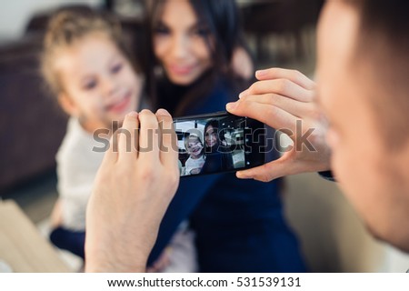 family, parenthood, technology, people concept - happy father taking photo of his little daughter and wife by smartphone having dinner at restaurant