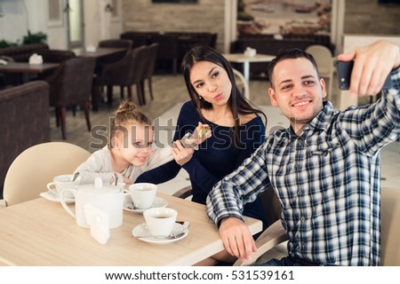family, parenthood, technology people concept - happy mother, father and little girl having dinner taking selfie by smartphone at restaurant