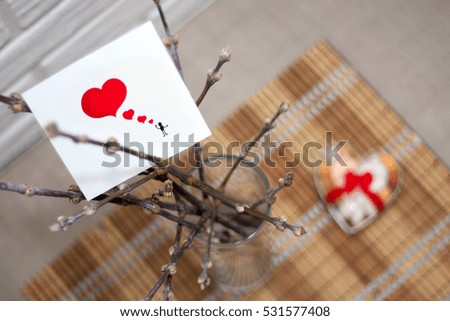 Colored love background with  drawn little man sending red hearts on a piece of paper card placed on branches in vase on linen fabric  cover with present out of focus on table in a room. Valentintines