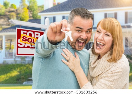 Happy Mixed Race Couple With Keys in Front of Sold For Sale Real Estate Sign and New House.