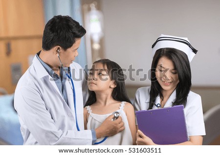 Male doctor examining little asian girl and nurse with background blur patient room.