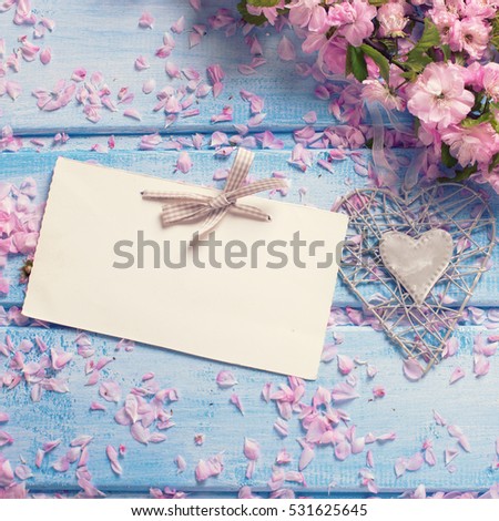 Background  with pink sakura  flowers and empty tag on blue wooden planks. Flat lay. Selective focus. Place for text. Square, toned image.