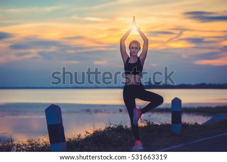 Silhouette of woman practicing yoga during sunset at riverside.