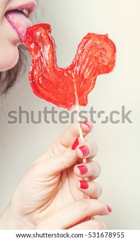 symbol 2017. Cute girl licking candy lollipop red rooster on a white background closeup
