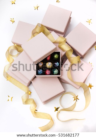 Chocolate hand painted luxury candy bonbons in a pink gift boxes and golden ribbon. White background with golden stars. 