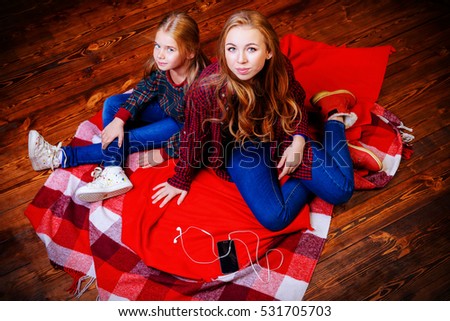 Family concept. Two cute girls, older and younger sister sitting together on a floor. Children's fashion.