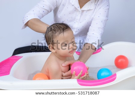 Happy baby taking a bath playing with mother washing little boy. baby girl playing with colored balls in the bath.