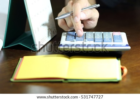Calculator, hand,pen,calendar and note book on dark brown desk,financial and education concept