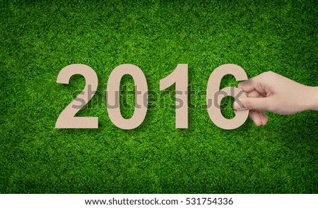 2016 Year - Hand holding paper cut of alphabet number on green grass background.