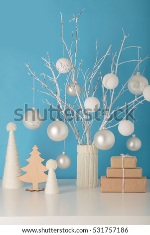 Vase in white knitted cover with white branches and Christmas toys. Christmas tree made of yarn and gifts