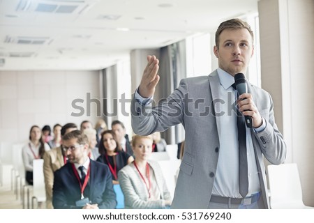 Businessman speaking through microphone during seminar in convention center Royalty-Free Stock Photo #531769240