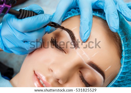 Cosmetologist applying permanent make up on eyebrows- eyebrow tattoo Royalty-Free Stock Photo #531825529