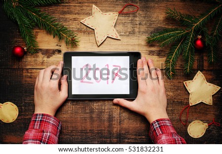 Child holding tablet PC in hands. Fir-tree branches with Christmas decorations and a text on a pad of 2017. Top view. Concept of New year