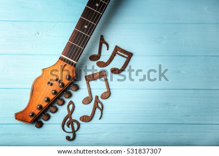 Guitar neck and music notes on color wooden background