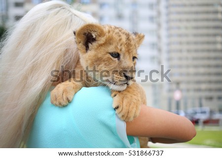 Blonde holds calf of lion on her shoulder outdoor, back view, close up