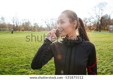 Picture of happy woman runner in warm clothes in autumn park talking by her phone