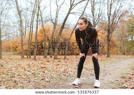 Picture of young woman runner in warm clothes and earphones running in autumn park
