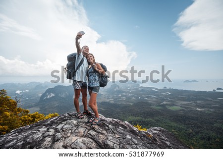 Couple of hikers taking selfie from top of the mountain with valley view on the background
