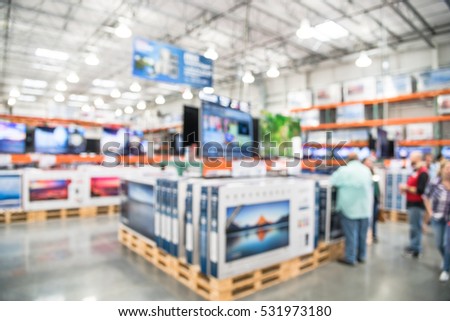 Electronic department store with bokeh blurred background. Television retail shop, TVs display on shelf at wholesale store. Defocused warehouse interior technology aisle, shelves and customer shopping Royalty-Free Stock Photo #531973180
