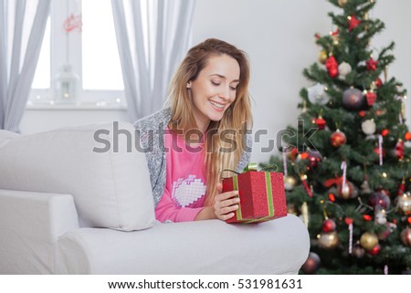 Beautiful happy young woman lying on the sofa holding a Christmas present