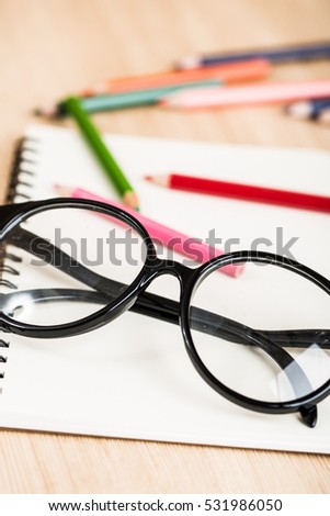 Eyeglasses with color pencil and blank notebook on student desk