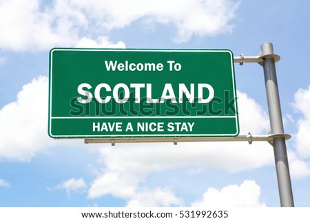 Green overhead road sign with a Welcome to Scotland, Have a Nice Stay concept against a partly cloudy sky background.