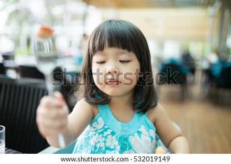 Happy little asian girl use fork and eating sausage on breakfast time.

