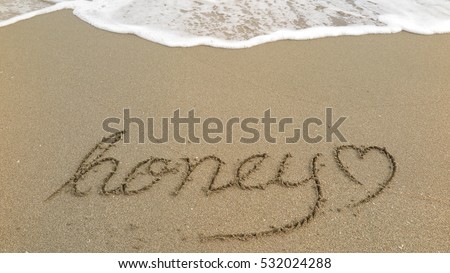 Handwriting words "honey" on sand of beach