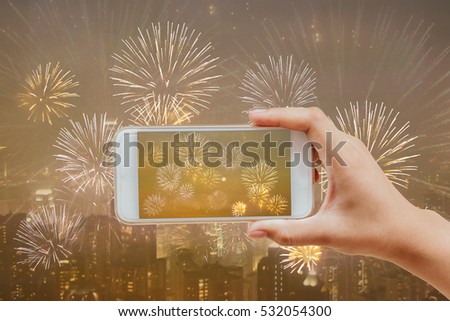 hand holding mobile smart phone taking picture of fireworks on blurred city night view for celebration holiday such as new year, independence day or anniversary 