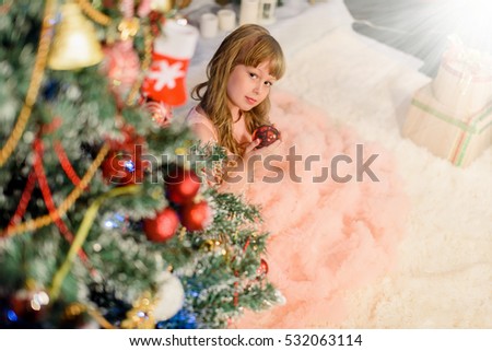 Little girl decorates christmass tree.