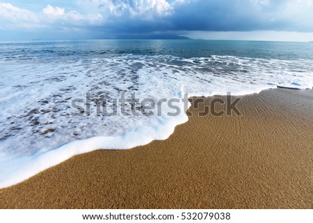 Soft wave of blue ocean on sandy beach. Background. Tropical snow on the sand. Empty beach with sea foam washing up from sea. Samui island, Thailand.