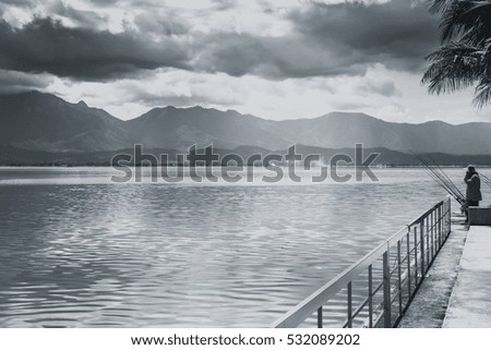 fisherman fishing at quiet lake with mountain sky and cloudy countryside black and white tone.