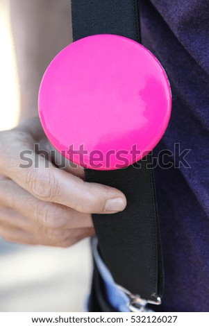 Person holding pink button attached to suspenders. Concept to add text or images to this blank button. 