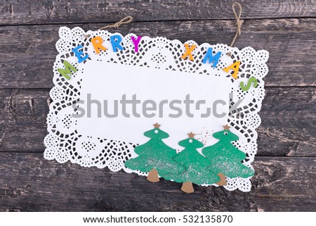 Merry Xmas greeting text written with small, colorful, wooden letters on a pure white napkin, placed on a wooden, vintage look background (rotated image)