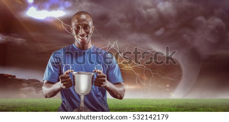 Portrait of happy athlete holding trophy against stormy sky with tornado over landscape 3D
