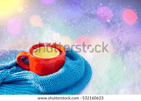 Mug of hot tea with a slice of lemon and a knitted scarf. Picturesque winter composition on the snow.