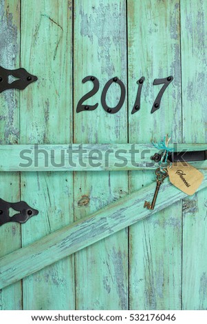 Year 2017 holiday sign in black iron numbers and skeleton house key with success tag on antique rustic mint green wood door; painted wooden copy space for text