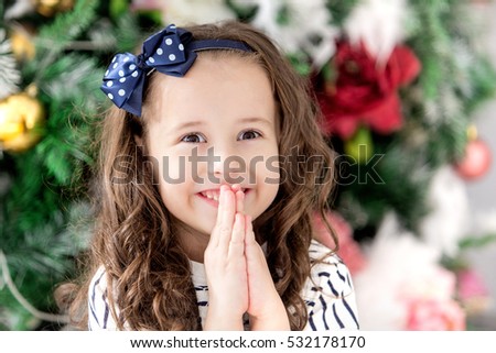 Close-up portrait of baby smiling girl which make a wish for the new year on the background of the Christmas tree. Holiday and fun. Happy baby girl. Merry Christmas. 2017 