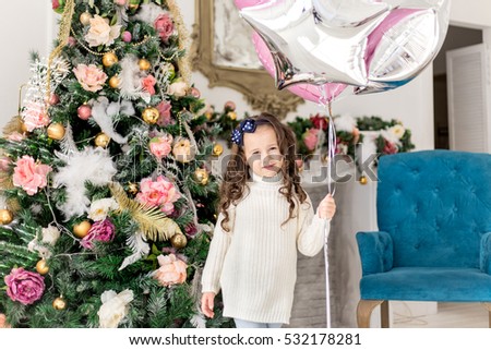?ute smiling little girl and sitting near the Christmas tree. New Year. Holiday and fun. Happy baby girl. Merry Christmas. 2017