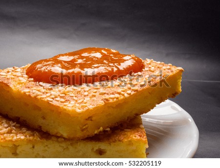 Slice of cheesecake with sesame seeds and apricot jam on a black background