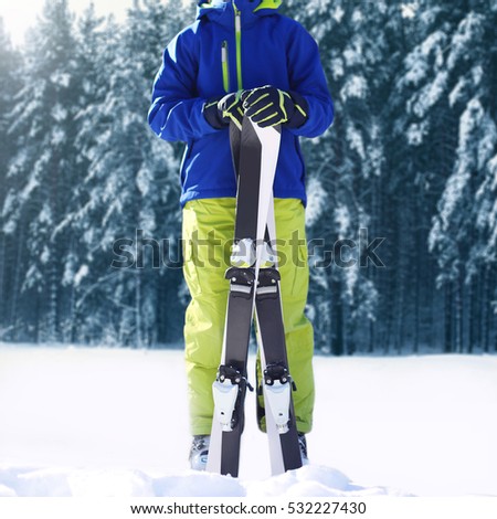 Winter skier teenager sportsman in sportswear with ski standing on snow over snowy forest background.