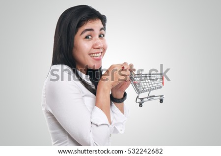Photo image portrait of a beautiful cute young Asian woman smiling while holding mini shopping trolley, consumer concept, side view half body close up portrait