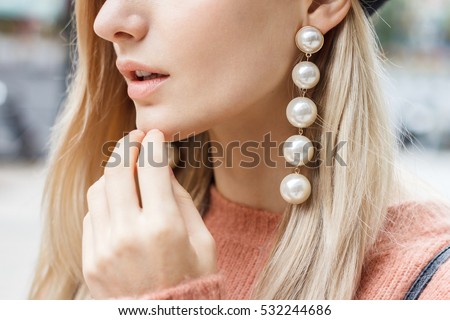 Close up detail of beautiful young blonde woman dressed in pink sweater with gorgeous earrings made of big pearls. 
